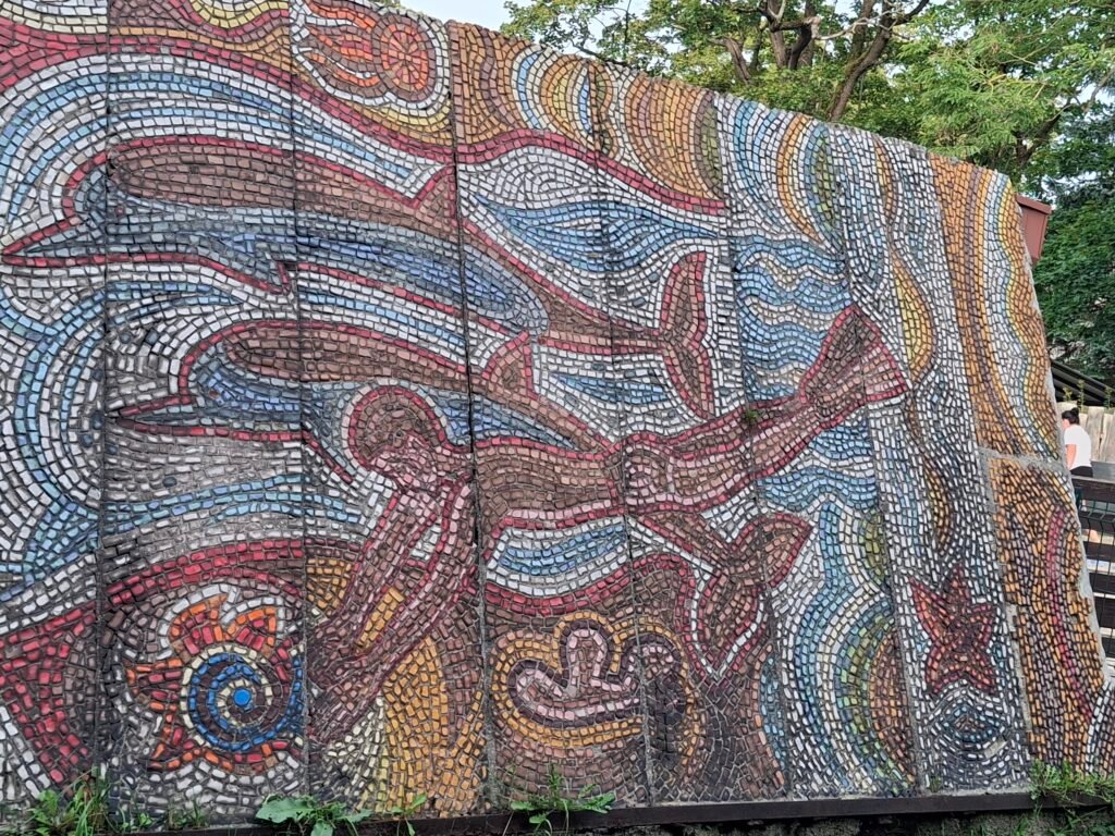 A large tiled mosaic wall with abstract flowing shapes in blue, red, and gold.